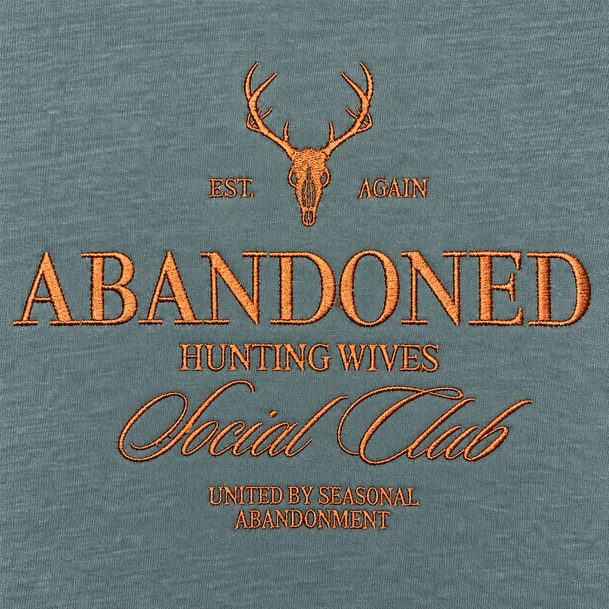 Close-up of copper brown Abandoned Hunting Wives Social Club embroidery on Blue Spruce sweatshirt